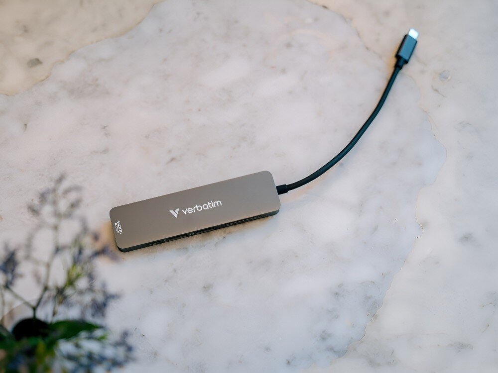 Hub Verbatim 32156 Niewielki hub USB-C z logo producenta leży na marmurowym blacie, z kablem zakończonym wtyczką widoczną po prawej stronie, 
            hub technologia dapter komptuer laptop