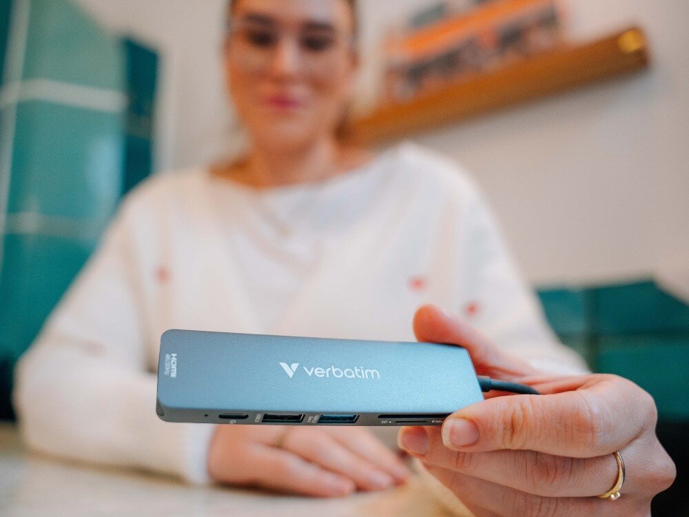 Hub Verbatim 32156 Osoba w jasnym swetrze trzyma w dłoni hub USB-C, pokazując jego porty skierowane w stronę aparatu, 
            hub usbc hdmi 3.2 gen1 power delivery pd sd microsd