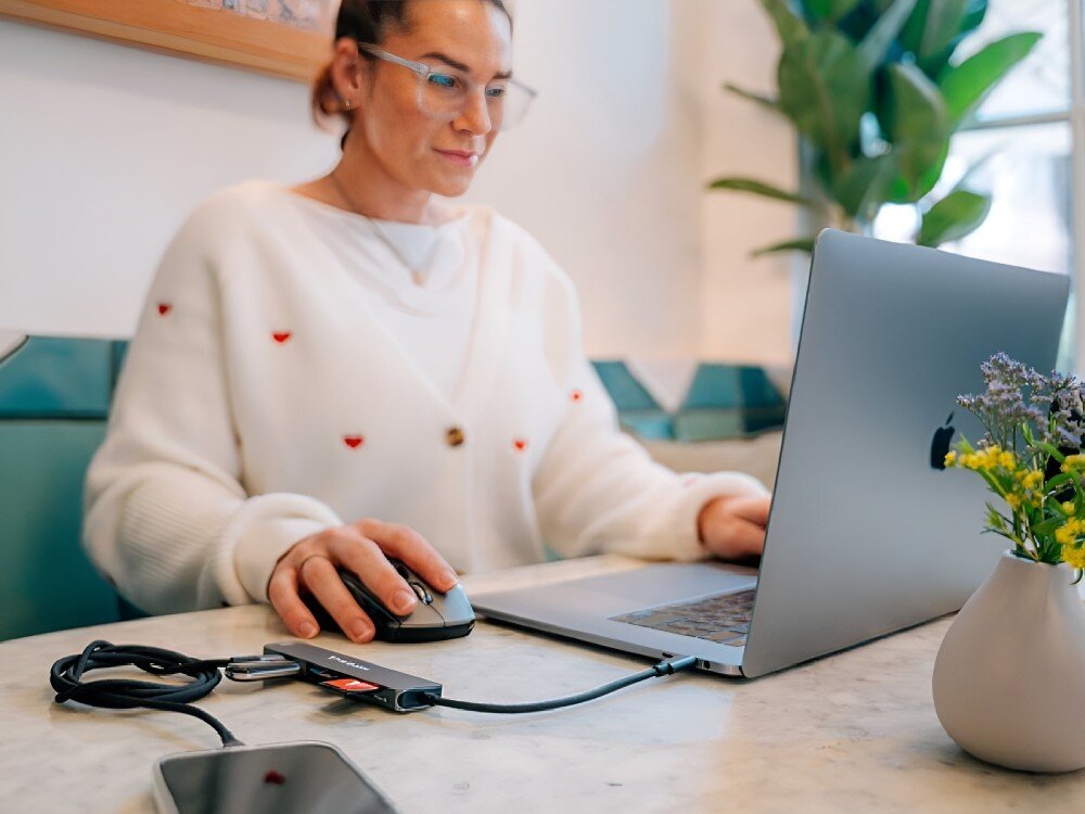 Hub Verbatim 32156 Osoba pracująca przy laptopie w kawiarni, używa myszki. Na stole widoczny jest podłączony hub USB-C z kilkoma urządzeniami, 
            hub hdmi 4k 30hz monitor grafika filmy