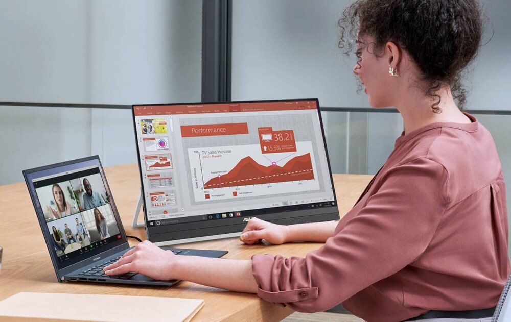 Monitor ASUS ZenScreen MB27ACF Kobieta siedząca przy biurku pracuje na laptopie i dodatkowym monitorze, na którym wyświetlona jest prezentacja z wykresami, opis