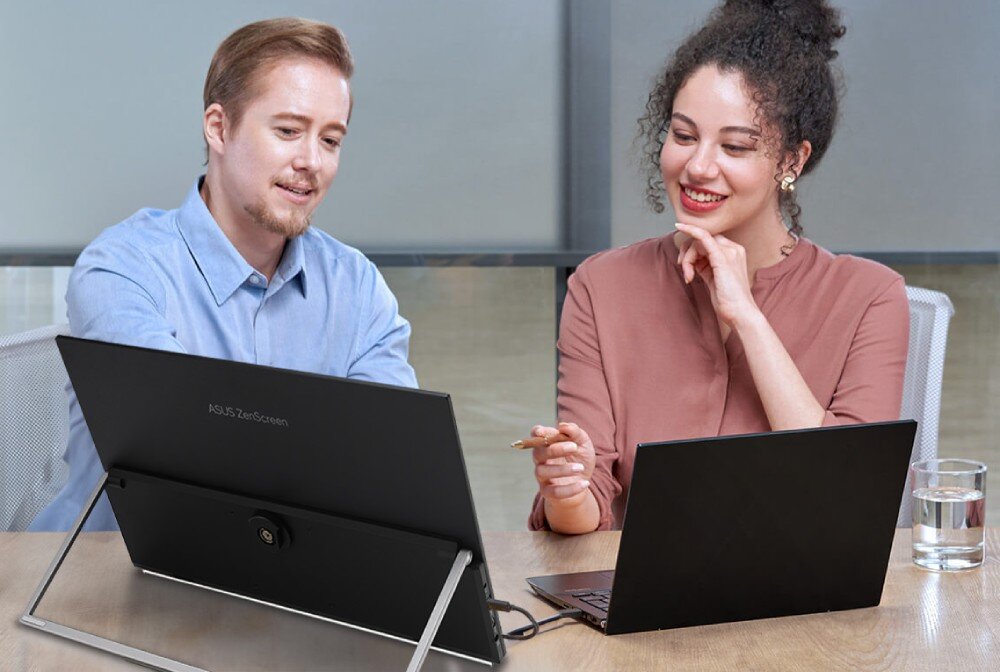 Monitor ASUS ZenScreen MB27ACF Kobieta i mężczyzna siedzą przy biurku, przed nimi stoi monitor podłączony do laptopa, oboje rozmawiają i uśmiechają się, rączka, podpórka, ustawienie, ergonomia, ramię