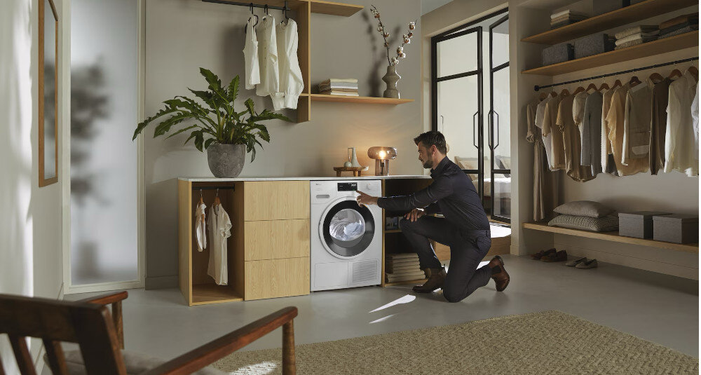 Suszarka MIELE TSH783WP EcoSpeed zdjęcie wizualizacyjne lifestyle pomieszczenie mężczyzna zmiana ustawień panel Optymalna ochrona domu optymalne wartości szczelności ochrona domu mebli pomieszczeń