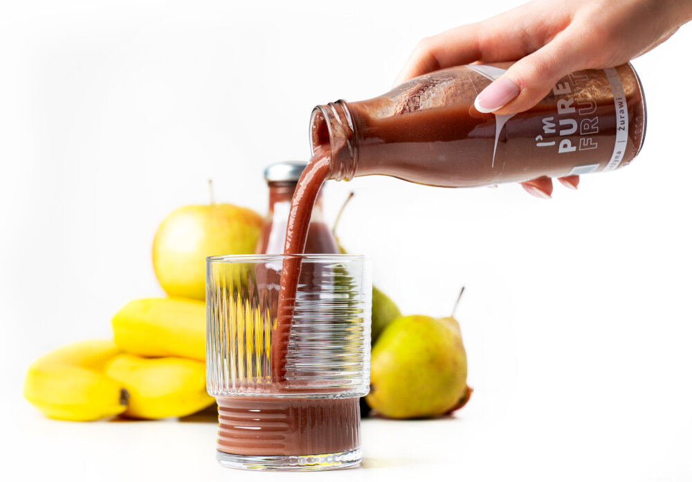 Sok COLLIBRE Pure Fruits Jeżynowo-gruszkowo-żurawinowy 15 x 250 ml osoba nalewa sok do szklanki w tle owoce zdjęcie na białym tle kompozycja jeżyny gruszki i żurawiny subtelną równowagą kwasowości i słodyczy banany i jabłka kremowa nuta w zestawie 15 butelek o pojemności 250 ml każda