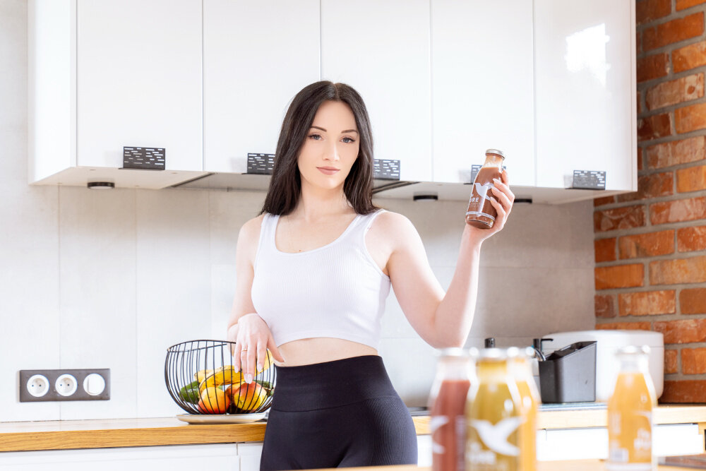 Sok COLLIBRE Pure Fruits Jeżynowo-gruszkowo-żurawinowy 15 x 250 ml kuchnia kobieta stoi przy blacie w dłoni trzyma butelkę soku sposób na dostarczenie organizmowi niezbędnych składników odżywczych w naturalnej formie powstaje z całych owoców i warzyw naturalnie bogaty w błonnik 2,6 g i składniki odżywcze