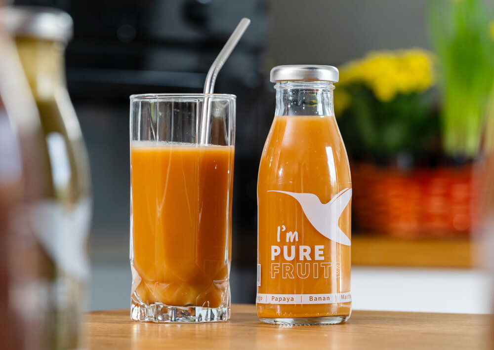 Sok COLLIBRE Pure Fruits Malinowo-porzeczkowo-borówkowy 15 x 250 ml butelka i szklanka wypełniona sokiem stoją na blacie z mango papayą i marchewką połączenie owoców i warzyw naturalny smak harmonia składników eksplozja świeżości składniki pochodzą z pełnowartościowych owoców i warzyw