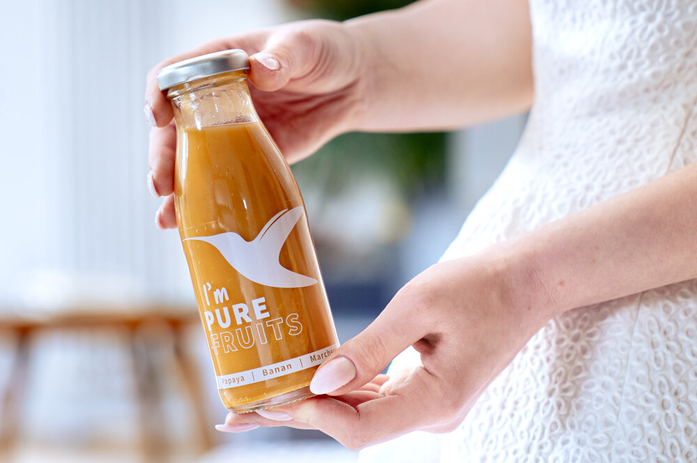 Sok COLLIBRE Pure Fruits Malinowo-porzeczkowo-borówkowy 15 x 250 ml osoba trzyma butelkę soku w dłoniach sok NFC nie z koncentratu proces pasteryzacji bez konserwantów i sztucznych dodatków wolny od cukru i barwników