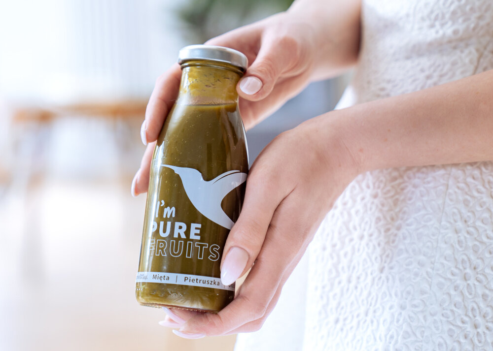 Sok COLLIBRE Pure Fruits Chlorella-mięta-pietruszka 15 x 250 ml osoba trzyma butelkę soku w dłoniach z chlorellą miętą i pietruszką połączenie owoców i warzyw delikatny smak z nutą orzeźwienia powstaje z całych owoców i warzyw bogaty w błonnik 0,9 g i składniki odżywcze