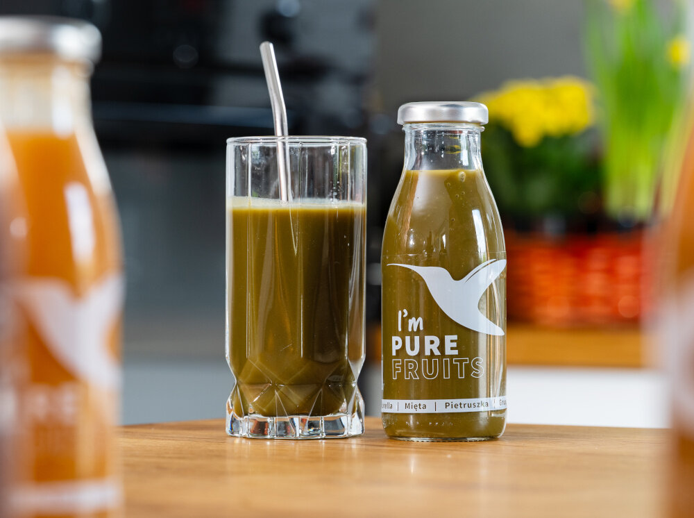 Sok COLLIBRE Pure Fruits Chlorella-mięta-pietruszka 15 x 250 ml butelka i szklanka wypełniona sokiem stoją na blacie chlorella 0,1% naturalna detoksykacja mięta 0,5% łagodzi układ trawienny pietruszka 16% dostarcza witamin A i E gęsty przecierowa forma