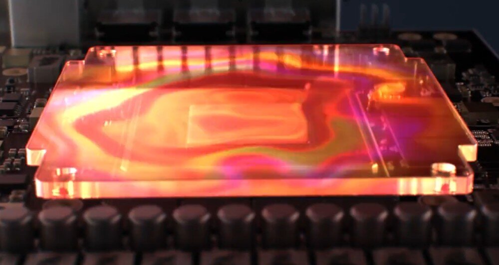 Karta graficzna ASUS TUF Gaming GeForce RTX 5070 OC Edition 12GB Zbliżenie na przezroczysty blok cieplny nałożony na układ scalony z widoczną iluminacją w odcieniach czerwieni i pomarańczy, odprowadzanie ciepła, podkładka termiczna, radiator