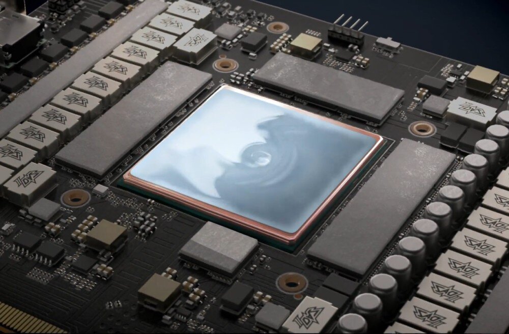 Karta graficzna ASUS Prime GeForce RTX 5070 OC 12GB Zbliżenie na układ graficzny z naniesioną srebrzystą warstwą pasty termoprzewodzącej. Wokół widoczne są komponenty płyty drukowanej, takie jak kondensatory i cewki, radiator, podkładka termiczna