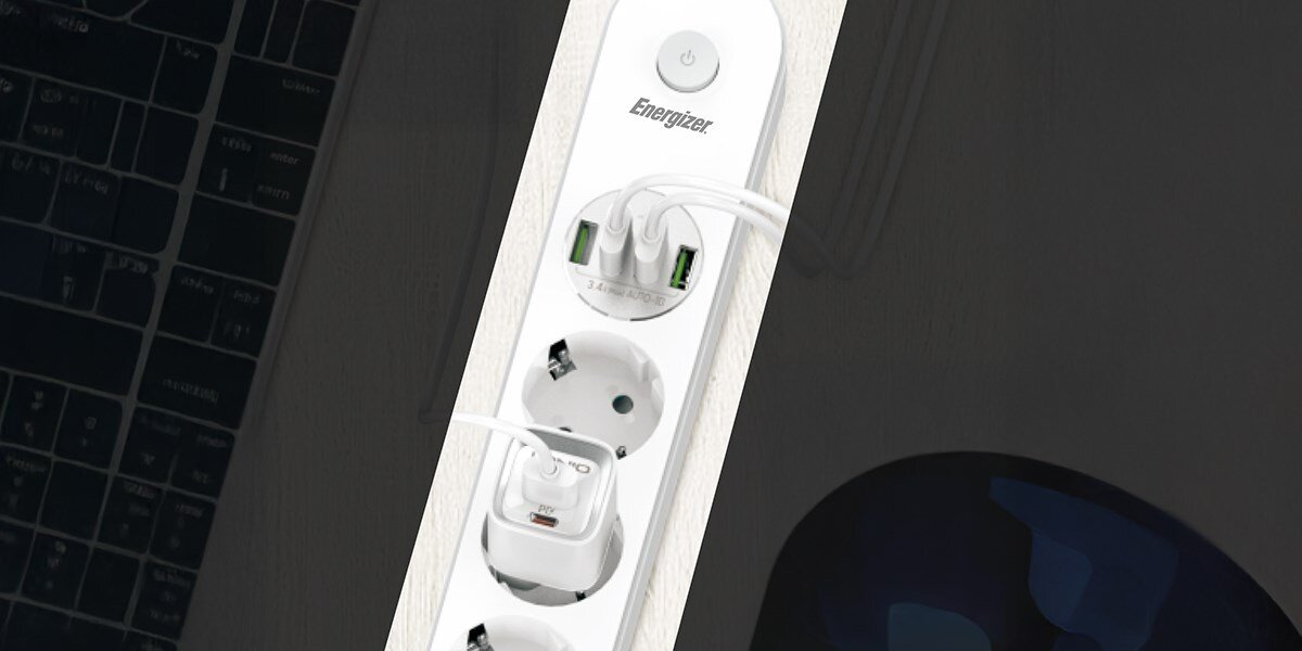 Listwa ENERGIZER EPB2500W00EU (2 m) biały Ujęcie z góry na czarno-szarą listwę zasilającą Energizer z trzema gniazdami i pięcioma portami USB z zielonymi diodami. Widoczny jest kabel zasilający i przycisk włącznika. Produkt jest ustawiony na ciemnym, szarym tle