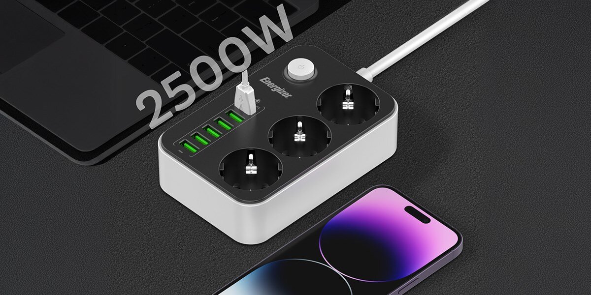 Listwa ENERGIZER EPB2500W01EU (2 m) Czarno-biały Listwa zasilająca Energizer z trzema gniazdami i portami USB, z jednym kablem USB podłączonym do smartfona leżącego na biurku. W tle widać laptopa. Duży biały napis '2500W' wskazuje na maksymalne obciążenie mocy