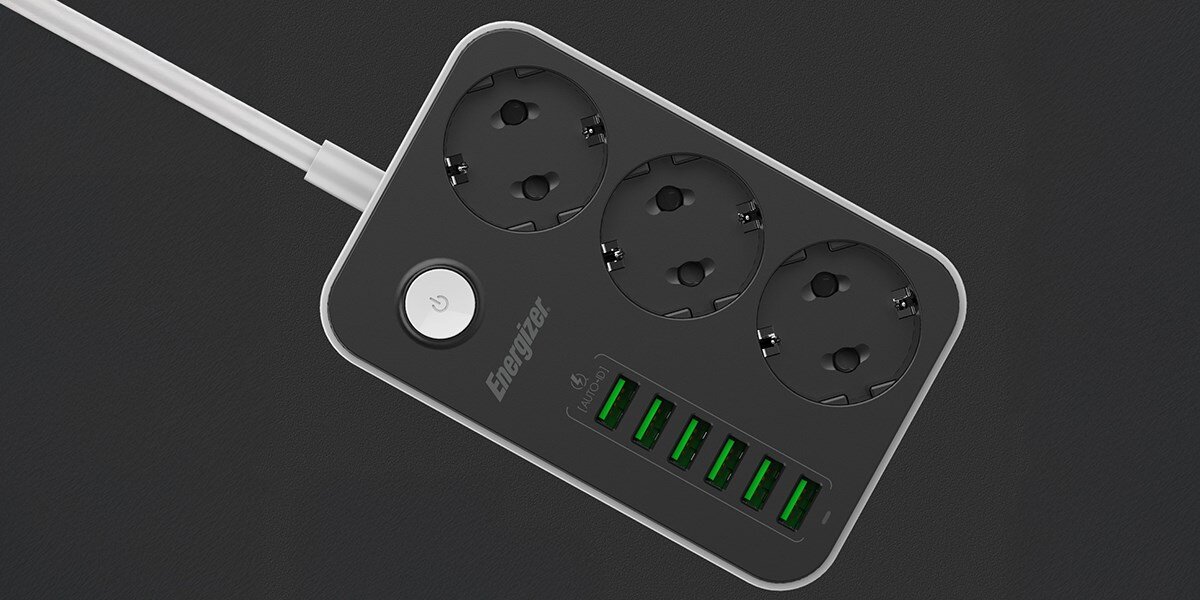 Listwa ENERGIZER EPB2500W01EU (2 m) Czarno-biały Ujęcie z góry na czarno-szarą listwę zasilającą Energizer z trzema gniazdami i pięcioma portami USB z zielonymi diodami. Widoczny jest kabel zasilający i przycisk włącznika. Produkt jest ustawiony na ciemnym, szarym tle