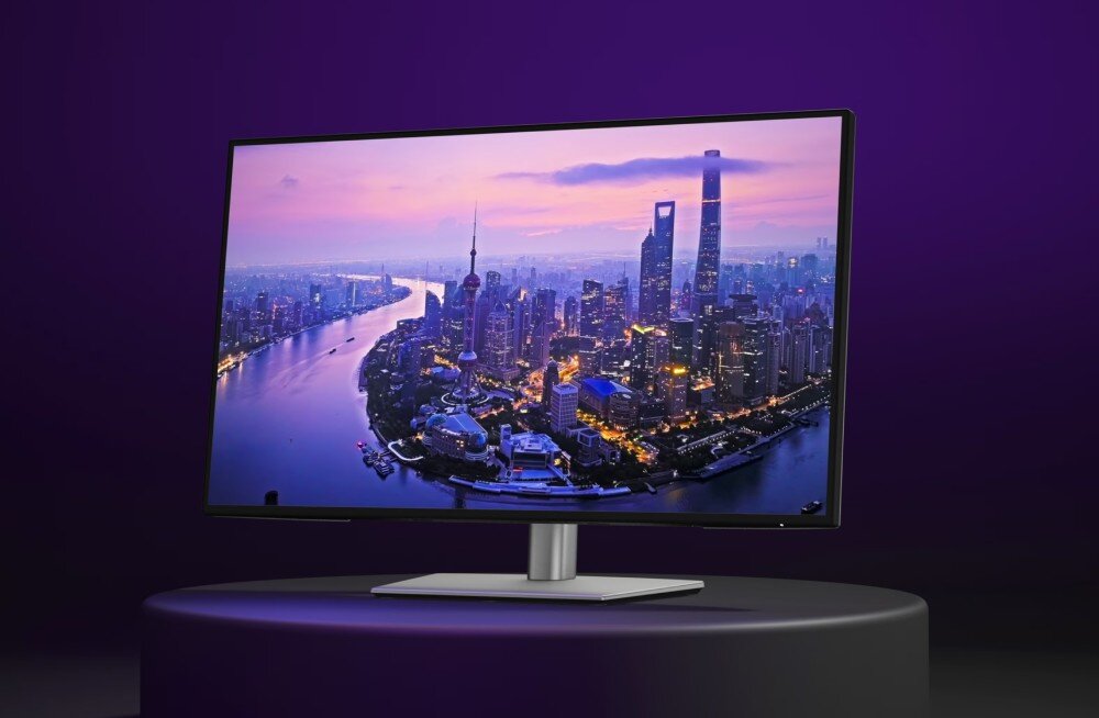 Monitor DELL UltraSharp U2725QE Monitor komputerowy z wyświetloną panoramą nocnego miasta na ekranie, stojący na okrągłym, czarnym podwyższeniu na fioletowym tle, opis