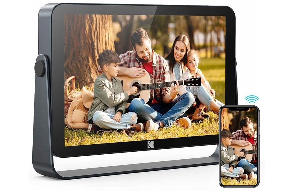 Ramka cyfrowa KODAK SB9782 Czarny prezentacja ramki ze zdjęciem przed nią telefon znak Wi-Fi aplikacja Kodak Digital Frame przesyłanie zdjęć i filmów z dowolnego miejsca na świecie