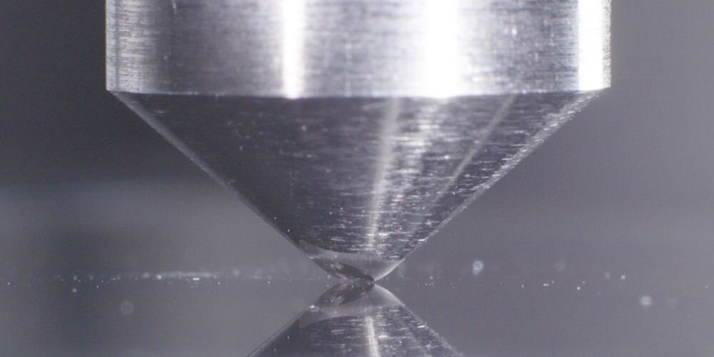 Zbliżenie na test wytrzymałości szkła Corning Gorilla Glass – diamentowa końcówka dociskana do powierzchni ekranu, symbolizująca odporność na zarysowania w laptopach ASUS VivoBook S 14 Flip. - Corning Gorilla Glass
