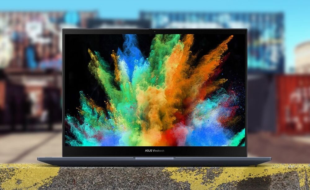 Laptop ASUS VivoBook S 14 Flip z ekranem prezentującym kolorowy wybuch farb proszkowych w odcieniach zieleni, niebieskiego i czerwonego, na tle miejskich kontenerów, podkreślający jakość i żywe kolory wyświetlacza. - 14-calowy, błyszczący ekran o rozdzielczości 1920 x 1200 px