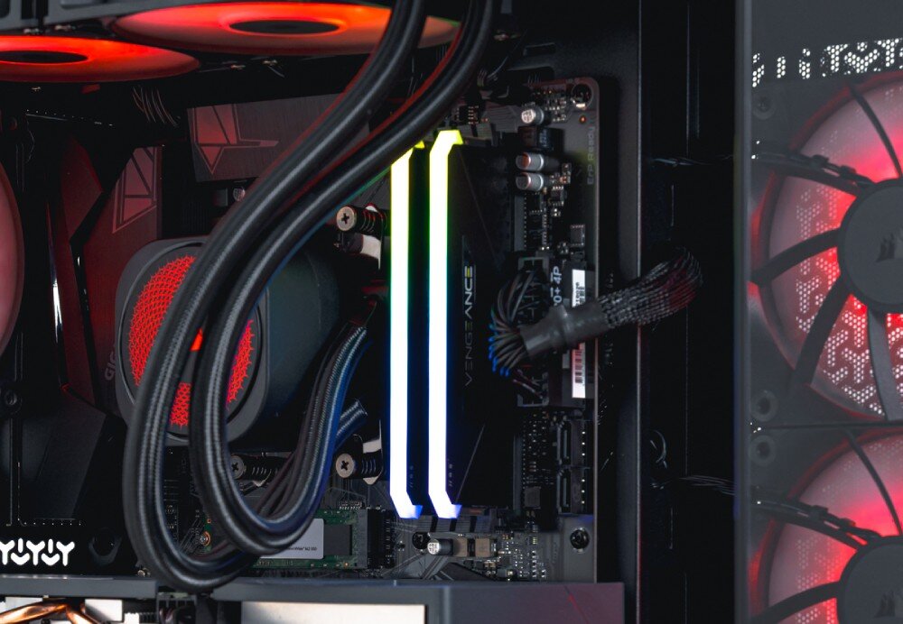 Komputer OPTIMUS E-sport GA550T-CR4 Zbliżenie na pamięć RAM z podświetleniem RGB oraz chłodzenie wodne w środku komputera. Widoczne także wentylatory w tle, pamięć RAM, płyta główna, karta sieciowa