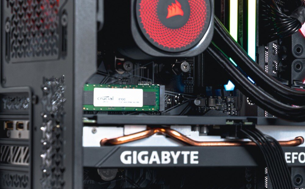 Komputer OPTIMUS E-sport GA550T-CR4 Zbliżenie na dysk SSD zamontowany pod chłodzeniem procesora. W tle widoczna karta graficzna i pamięć RAM z podświetleniem, dysk, pojemność, szybkość