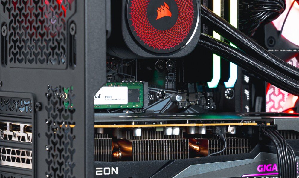 Komputer OPTIMUS E-sport GA550T-CR5 Zbliżenie na dysk SSD zamontowany pod chłodzeniem procesora. W tle widoczna karta graficzna i pamięć RAM z podświetleniem, dysk, pojemność, szybkość