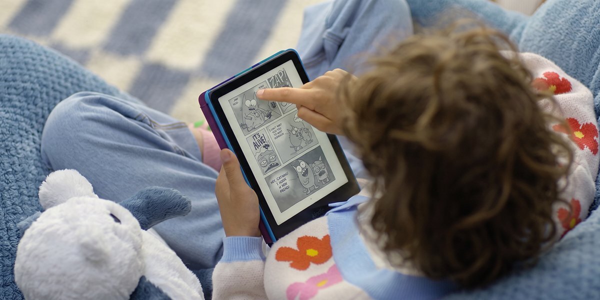Dziecko siedzi na fotelu, trzymając czytnik e-booków z wyświetlonym komiksem. Obok leży pluszowa zabawka.
