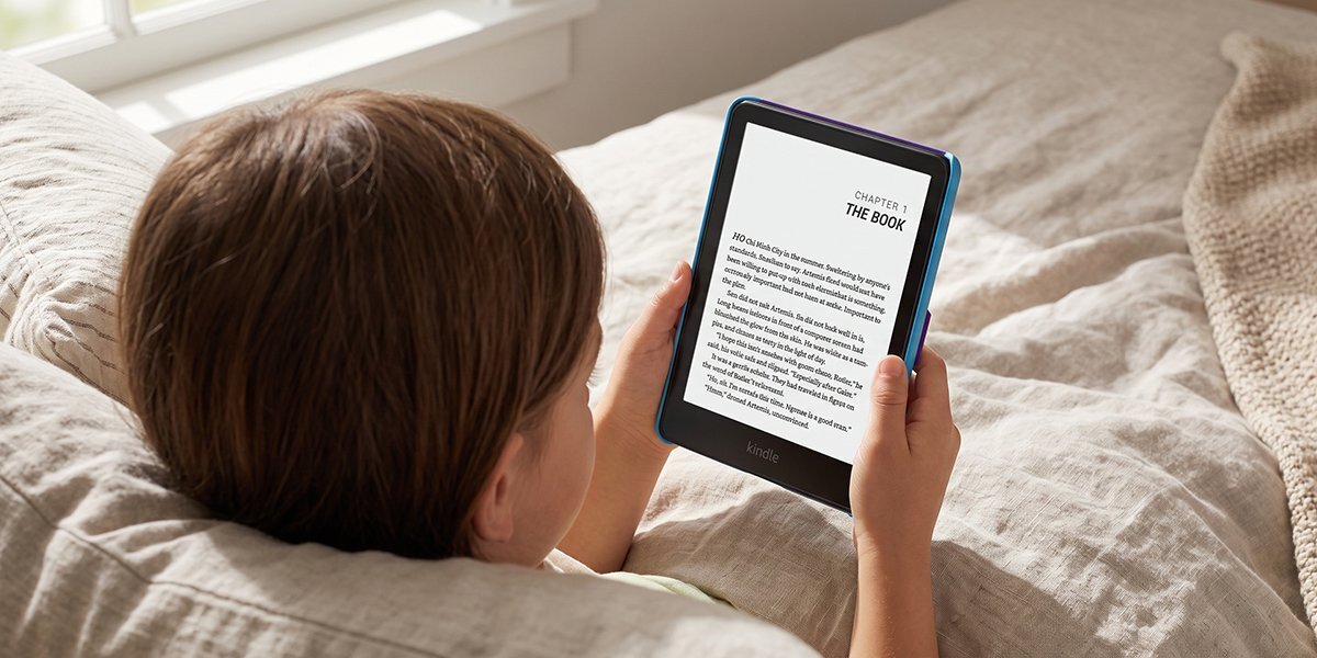Osoba trzyma czytnik e-booków z widocznym tekstem na ekranie: \'CHAPTER 1 THE BOOK\'.