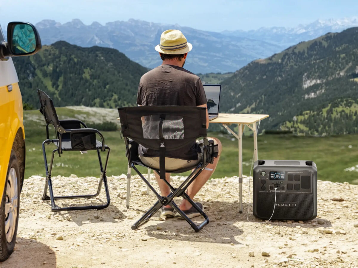 Stacja zasilania BLUETTI AC200L 2048 Wh Bank energii, prąd, zasilanie, energia, moc, w tle teren górzysty, na pierwszym palnie mężczyzna obserwuje obraz gór, obok stacja zasilania