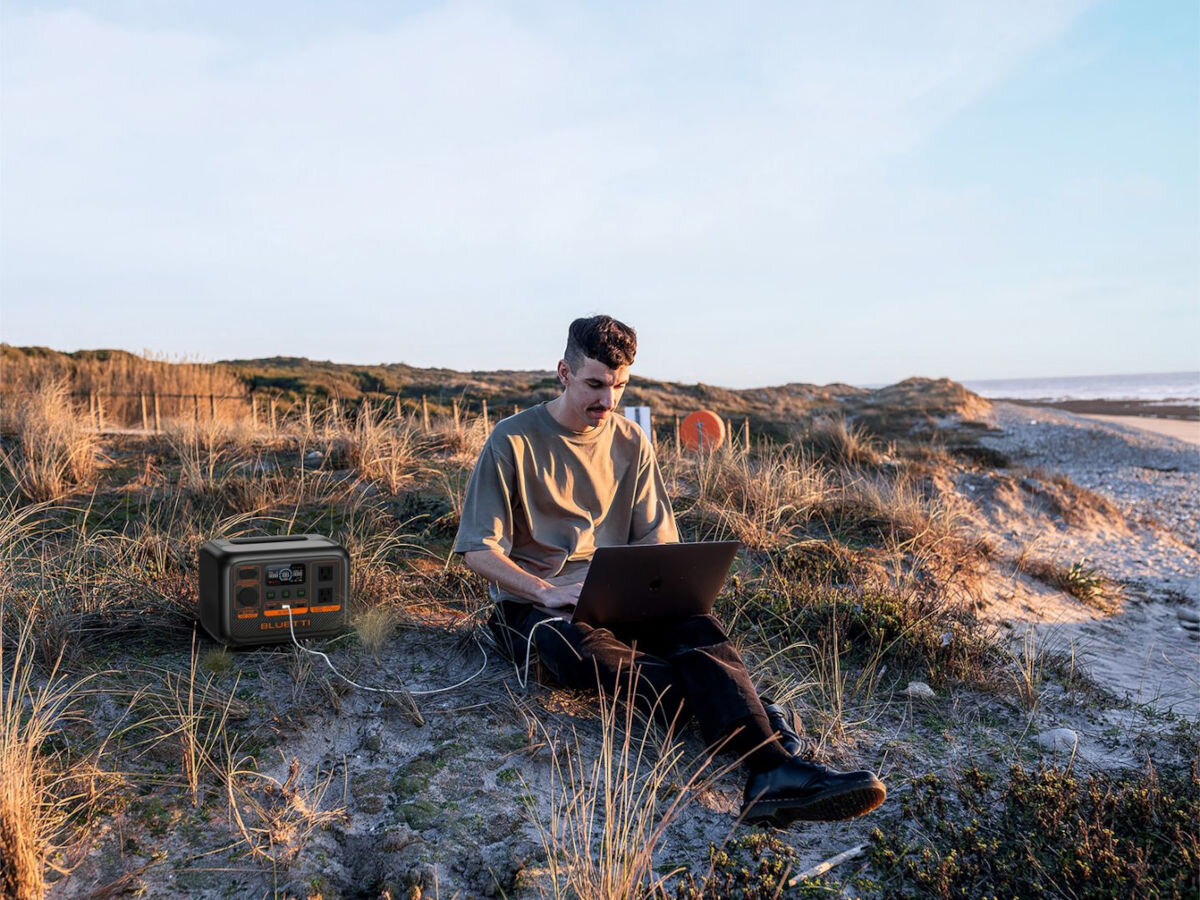 Stacja zasilania BLUETTI AC70P 864 Wh Bank energii, laptopy, porty, USB, power lifting, mężczyzna siedzi z laptopem nad morzem