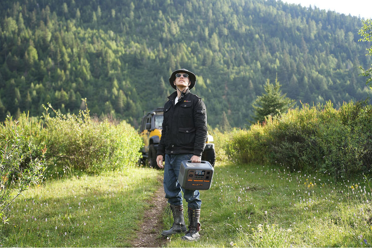 Stacja zasilania BLUETTI AC70P 864 Wh Bank energii, technologia, 45, naładowanie, panele, mężczyzna stoi w górzystym terenie, spogląda w górę trzymając stację zasilania