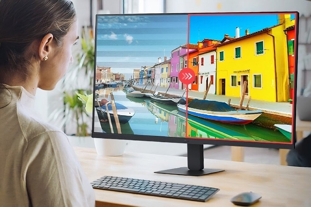 Monitor LG 32U631A-B Kobieta siedząca przy biurku, patrzy na ekran monitora. Połowa ekranu przedstawia wyblakły obraz miasta nad wodą, a druga połowa żywe, nasycone kolory tej samej sceny, ochrona wzroku, migotanie