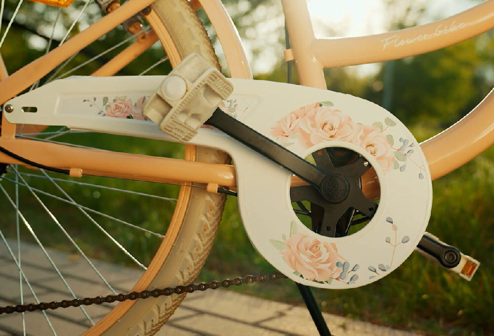 Rower młodzieżowy SUN BABY Flower Bike 24 cale dla dziewczynki Morelowy zbliżenie na osłonę łańcucha w tle trawa osłona łańcucha kwiatowa grafika zabezpiecza łańcuch przed brudem błotniki elegancki wygląd osłaniają odzież