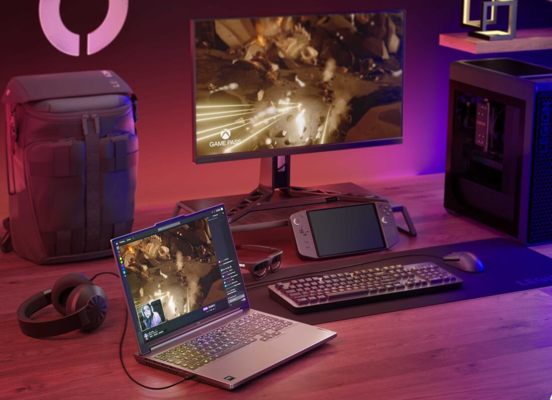 Gamingowe stanowisko z laptopem Lenovo Legion Slim 5 podłączonym do monitora z wyświetloną grą z Xbox Game Pass, na biurku klawiatura, mysz, słuchawki, konsola przenośna, plecak Lenovo Legion i komputer stacjonarny z podświetleniem RGB, całość w fioletowo-czerwonym świetle LED. - Wi-Fi 6E i Bluetooth 5.3