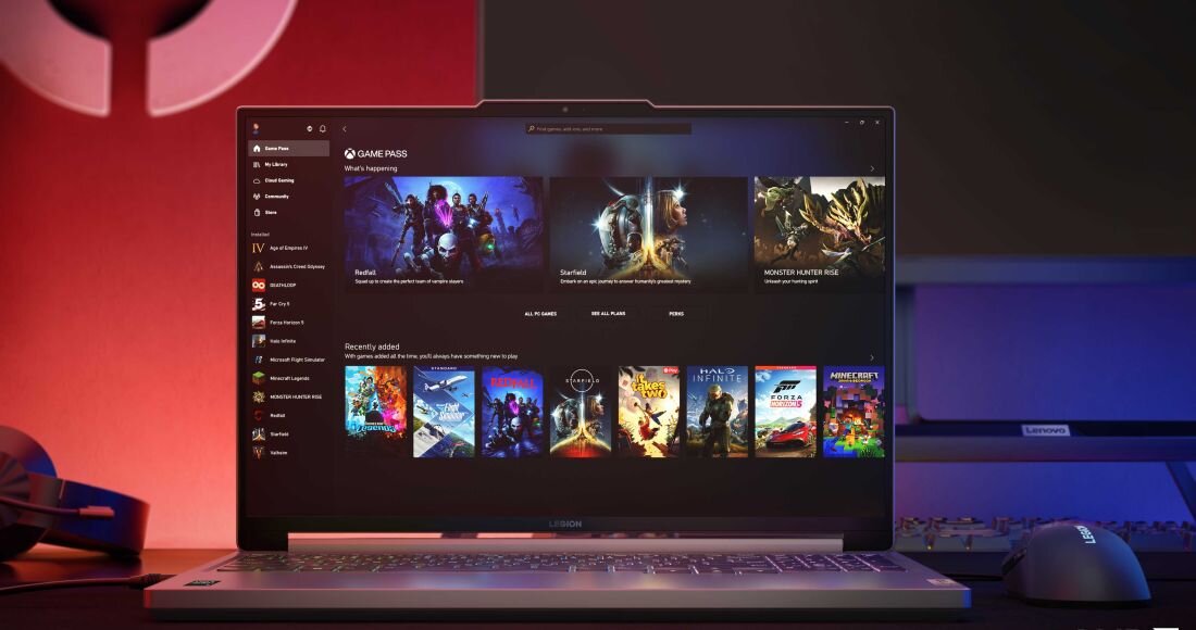 Laptop Lenovo Legion Slim 5 ustawiony na biurku gamingowym, ekran prezentuje interfejs Xbox Game Pass z grami, w tle czerwone podświetlenie i akcesoria gamingowe, po prawej widoczna mysz Lenovo Legion.