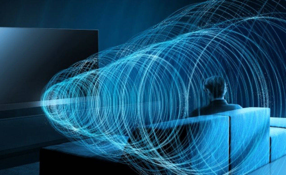 Telewizor PANASONIC TV77Z93AEG głośniki Array system dźwięk precyzyjny strefy, osoba siedząca na kanapie wpatrzona w telewizor otoczona dźwiękiem