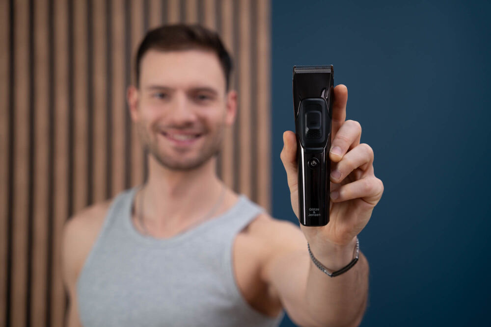 Strzyżarka GÖTZE & JENSEN CL950 Mężczyzna trzymający czarną strzyżarkę Götze & Jensen CL950 skierowaną w stronę obiektywu.