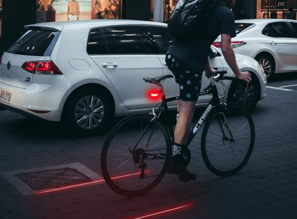 Lampka rowerowa EXTRALINK 14498 miasto ulica osoba jedzie na rowerze po drodze widok od tyłu wokól samochody budynki 5 mocnych diod LED o mocy 120 lm intensywne światło poprawia orientację w ruchu ulicznym wspiera bezpieczne poruszanie się po zmroku