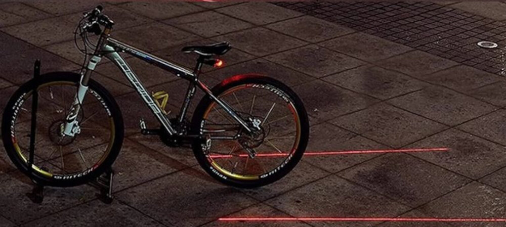 Lampka rowerowa EXTRALINK 14498 dwa zdjęcia z rowerami zbliżenie na wyznaczone linie przez laser system laserowy wyznacza wyraźne linie po obu stronach roweru linie sygnalizują szerokość roweru odpowiedni odstęp podczas wyprzedzania bezpieczna jazda