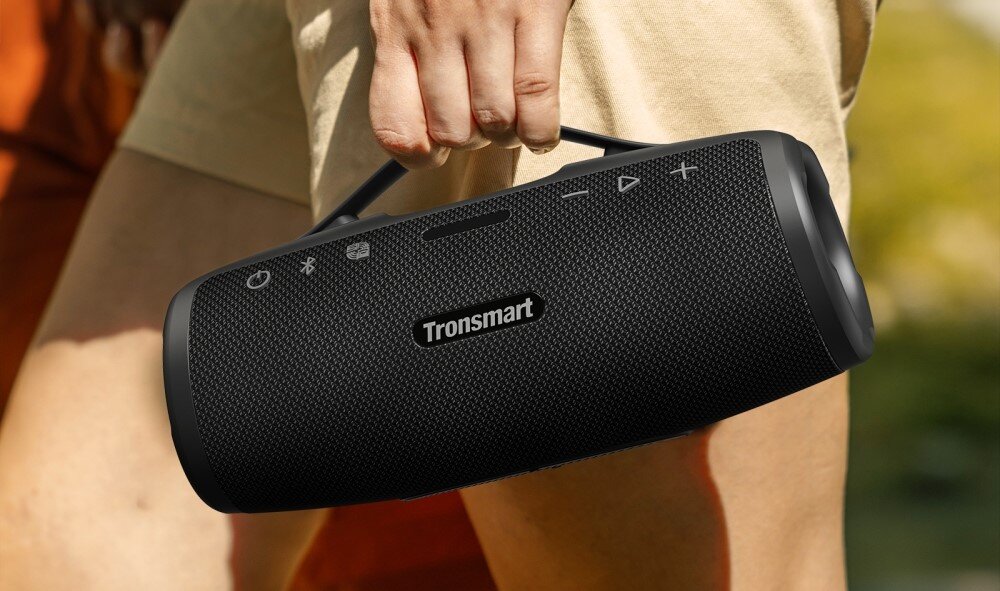 Głośnik TRONSMART Mirtune S100 przenośny Bluetooth wodoodporny, osoba trzymająca głośnik za uchwyt