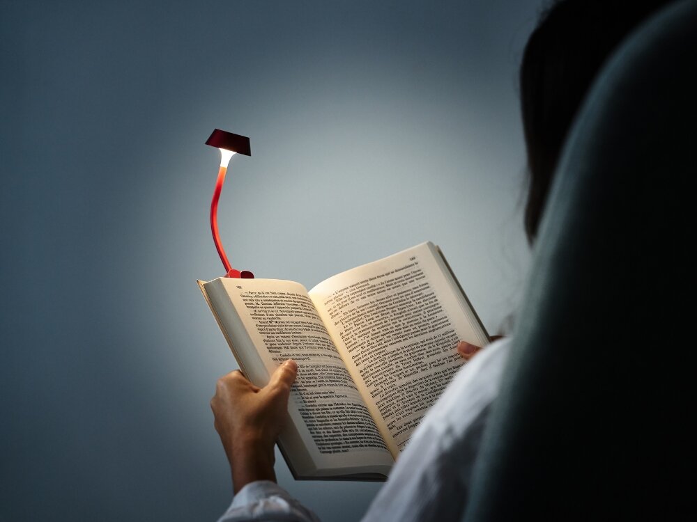 Lampka LED LEXON Mimi Ciemnoczerwony osoba trzyma książkę wpięta czerwona lampka do codziennego oświetlenia stylowy design praktyczność elastyczne ramię klips na książce biurku półce do domu biura w podróży dobre światło 