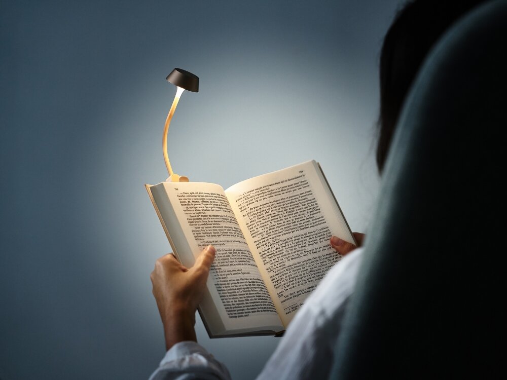 Lampka LED LEXON Mimi Złoty osoba trzyma książkę wpięta złota lampka do codziennego oświetlenia stylowy design praktyczność elastyczne ramię klips na książce biurku półce do domu biura w podróży dobre światło