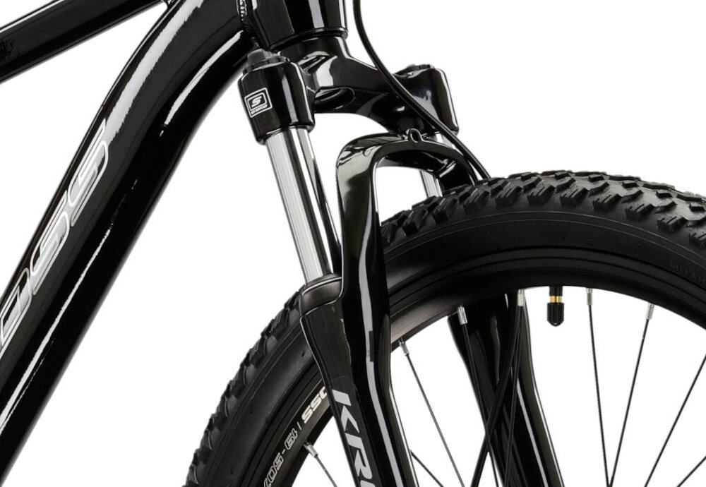Zbliżenie na przednie koło czarnego roweru z widocznym amortyzatorem i oponą z wyraźnym bieżnikiem. Na ramie roweru widoczny jest napis \'KROSS\'.