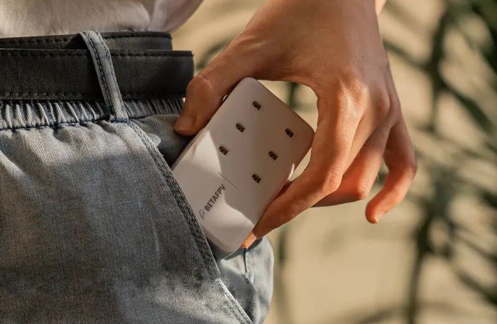 Hub BETAFPV 6 Ports 1S Zbliżenie na dłoń wsuwającą białe prostokątne urządzenie do ładowania do kieszeni jasnych spodni jeansowych