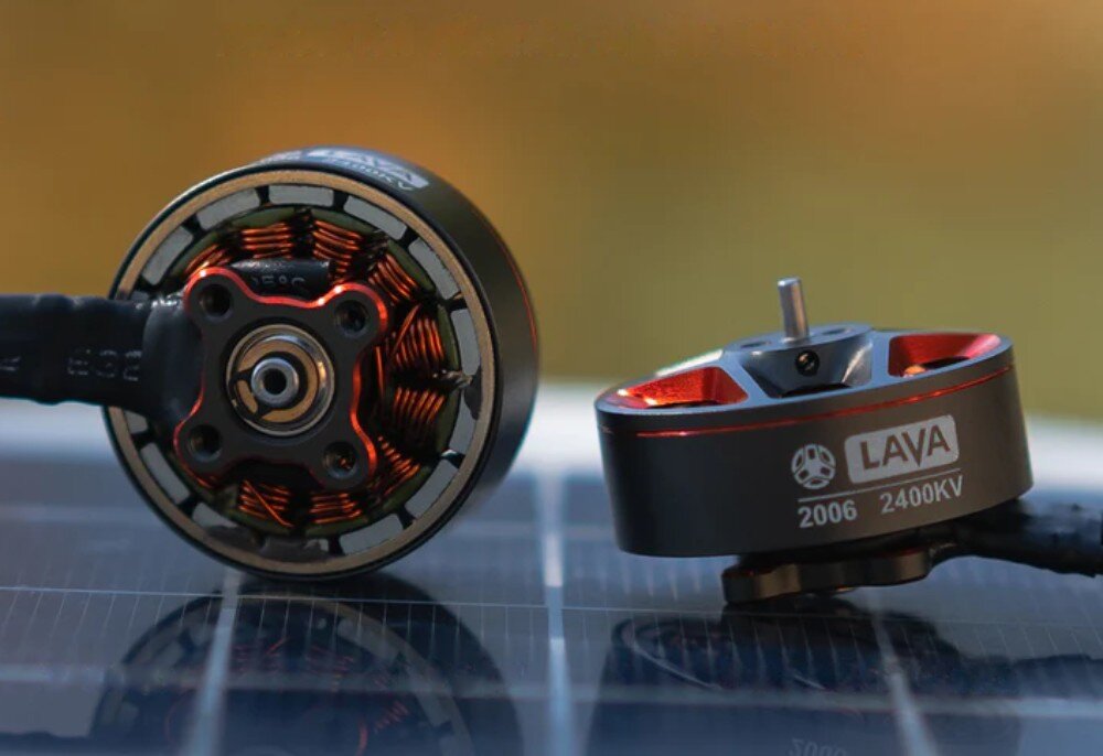 Silnik BETAFPV 2006-2400KV (1 szt.) Dwa silniki umieszczone na ciemnej i gładkiej powierzchni odbijającej światło, prezentujące zarówno spód z uzwojeniem jak i górną część z wałem napędowym