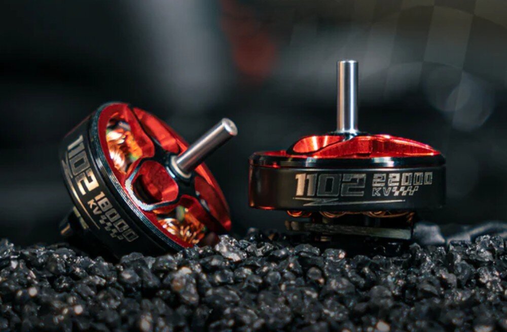 Silnik BETAFPV 1102 18000KV (4 szt.) Dwa silniki modelarskie umieszczone na czarnym żwirze, z których jeden leży na boku ukazując czerwone wnętrze i fragment napisu '18000KV', a drugi stoi pionowo z widocznym oznaczeniem '22000KV'