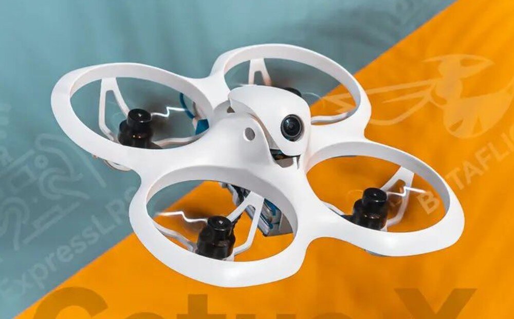 Rama BETAFPV Cetus X Frame Zmontowany biały dron z czarnymi silnikami i kamerą na froncie, leżący na tle podzielonym ukośnie na część niebieską i żółtą z logo BETAFPV