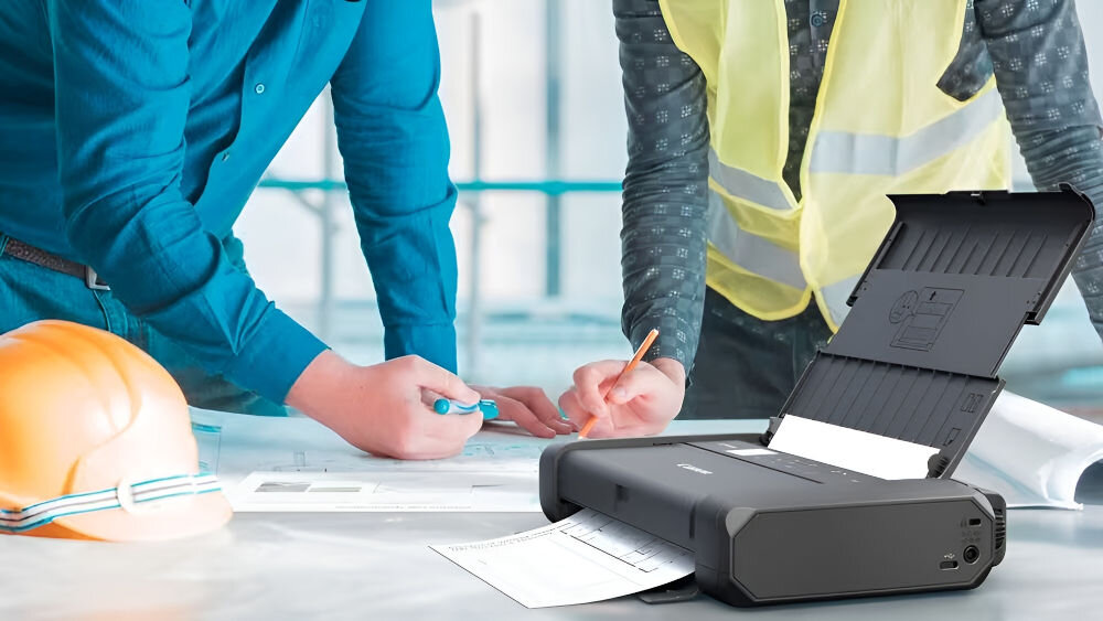 Drukarka CANON Maxify BX110 Druk w kolorze, Wi-Fi + Akumulator drukarka postawiona na stole kask leżący obok mężczyźni stojący przy biurku jeden w koszuli drugi w kamizelce odblaskowej mobilna konstrukcja branże pracujące poza biurem budowy logistyka praca administracji publicznej wytrzymała obudowa zasilanie akumulatorowe centrum dokumentacji