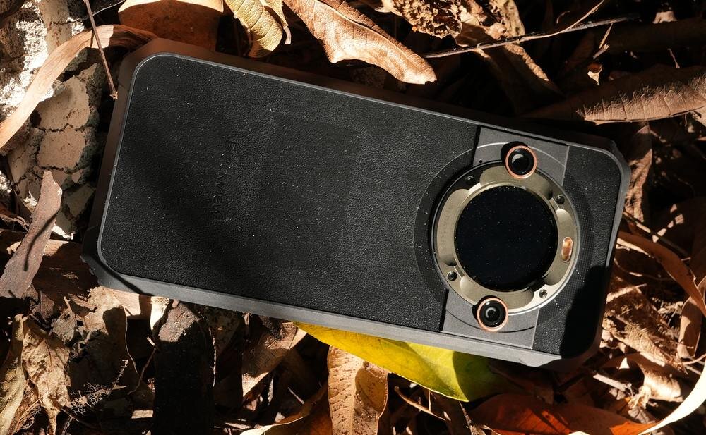 Czarny smartfon z okrągłym modułem aparatu, leżący na suchych liściach. Na obudowie widoczne jest logo \'BLACKVIEW\'.