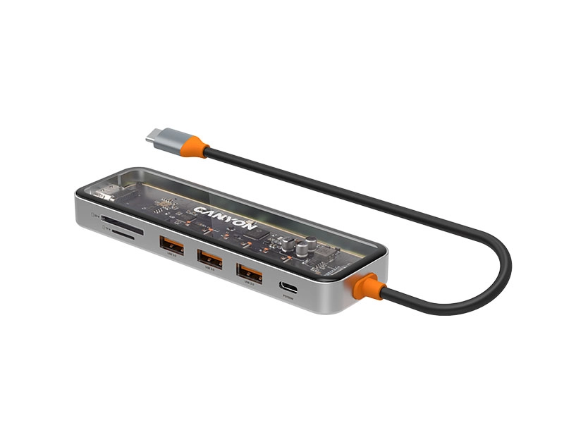 Przezroczysty hub USB-C z widocznymi elementami elektronicznymi i logo \'CANYON\'. Posiada kilka portów USB, slot na karty pamięci oraz kabel z pomarańczowymi akcentami.