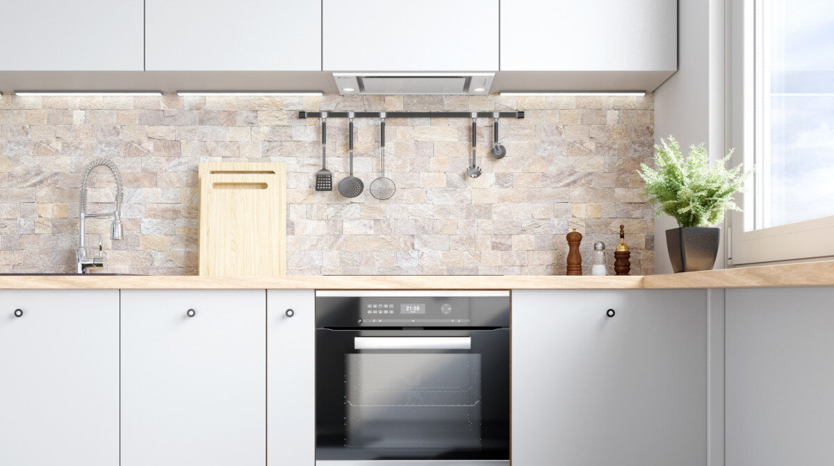 Okap GLOBALO Desolero 90.2 Biały Stylowa, jasna kuchnia z piekarnikiem do zabudowy, drewnianym blatem, kamienną ścianą i wiszącymi akcesoriami kuchennymi nad blatem