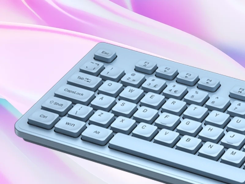 Na obrazie widoczna jest niebieska klawiatura z wyraźnie oznaczonymi klawiszami, takimi jak \'Esc\', \'Tab\', \'CapsLock\', \'Shift\', \'Ctrl\', \'Win\', \'Alt\'. Tło jest w pastelowych odcieniach różu i fioletu.